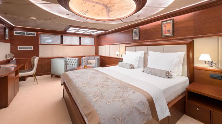 A luxurious master stateroom with king size bed, sitting area, desk and a decorative designer lamp.